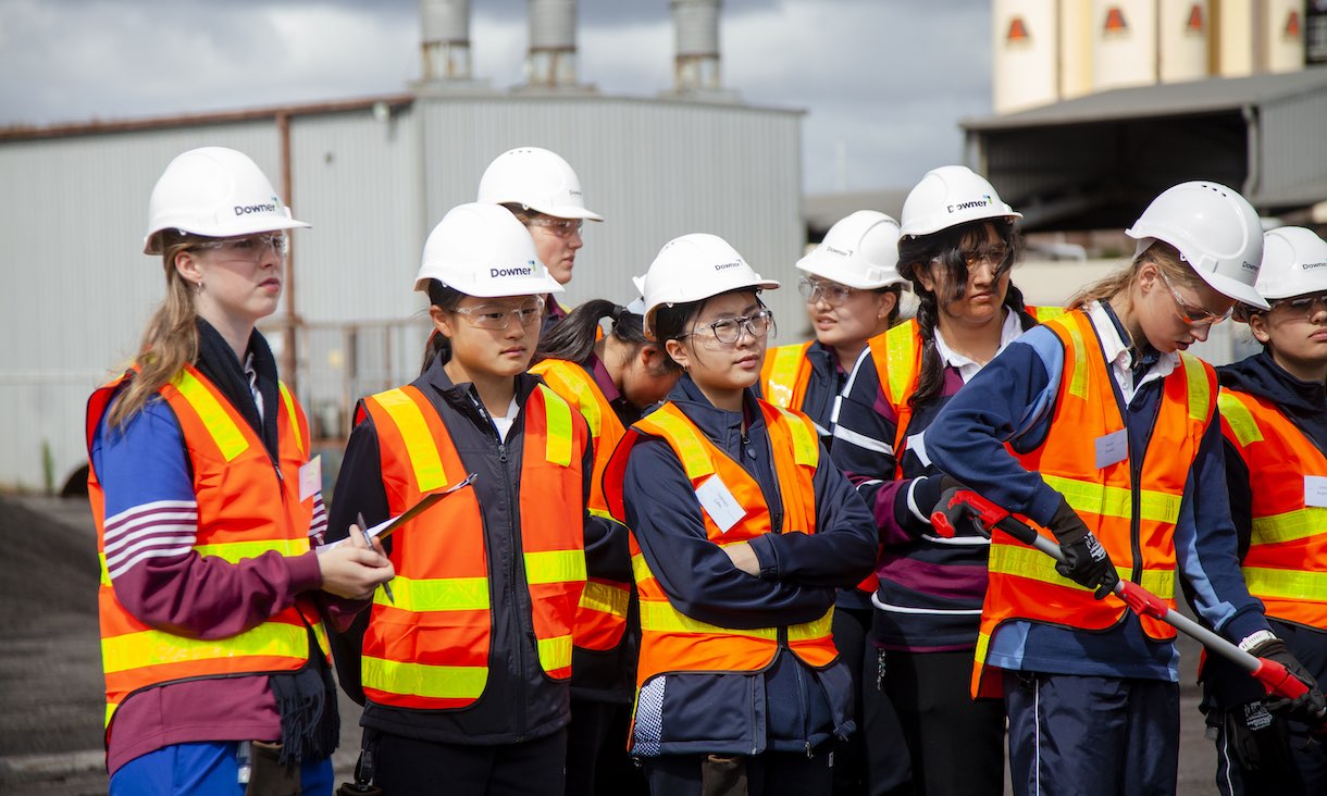 group of female high school students wearing high vis vests and hard hats on excursion at asphalt plant