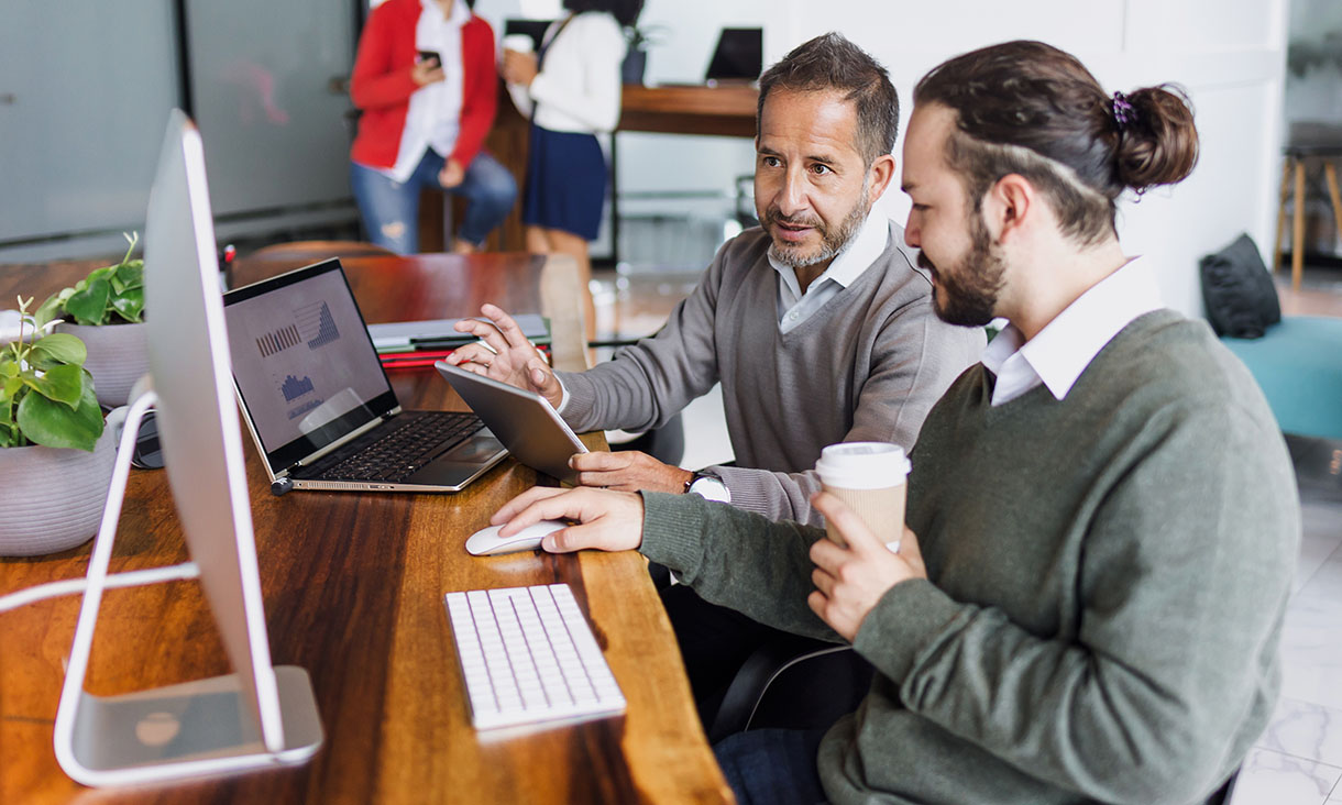 Two male employees working at a desk looking at the same laptop