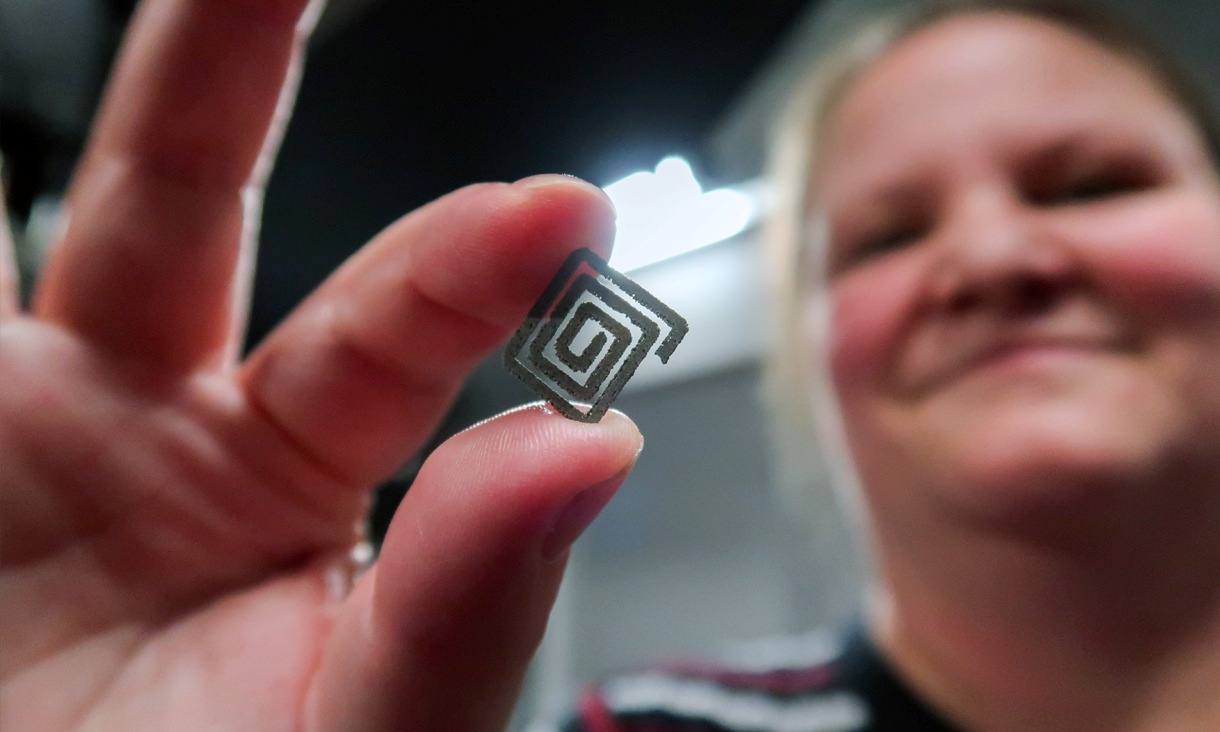 A woman holds a small square spiral-shaped diamond–titanium device between her fingers.