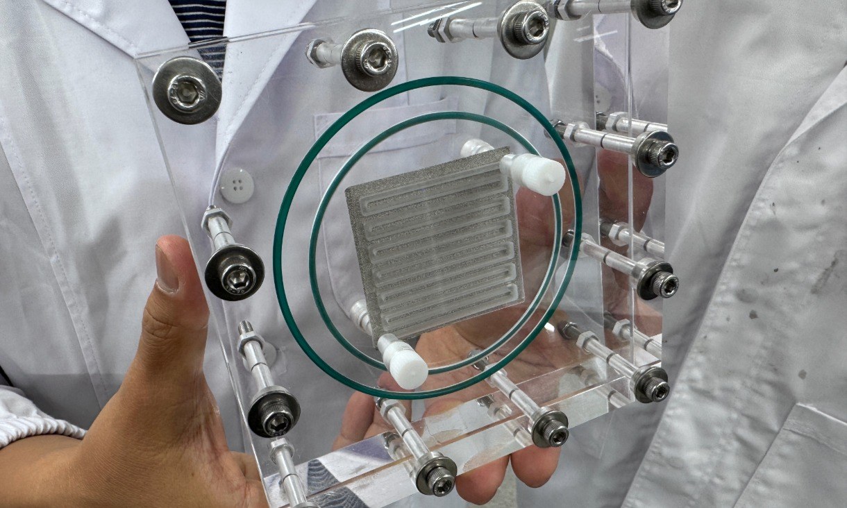 A transparent, square device with metal bolts and a circular green seal.