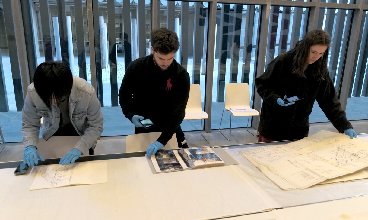 Three students wearing blue gloves photographing design papers. 