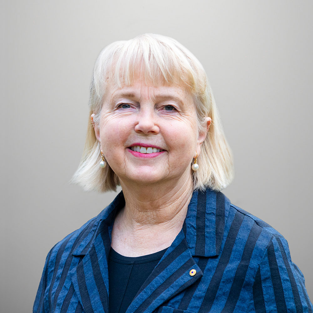 Peggy is smiling towards the camera against solid white background. Peggy is wearing a navy blue shirt.