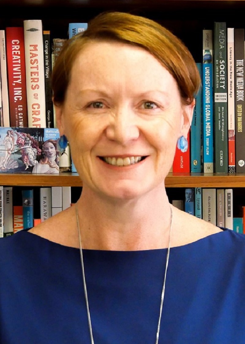 Susan Luckman headshot, Caucasion woman, short brown hair, smiling, in front of bookshelf 