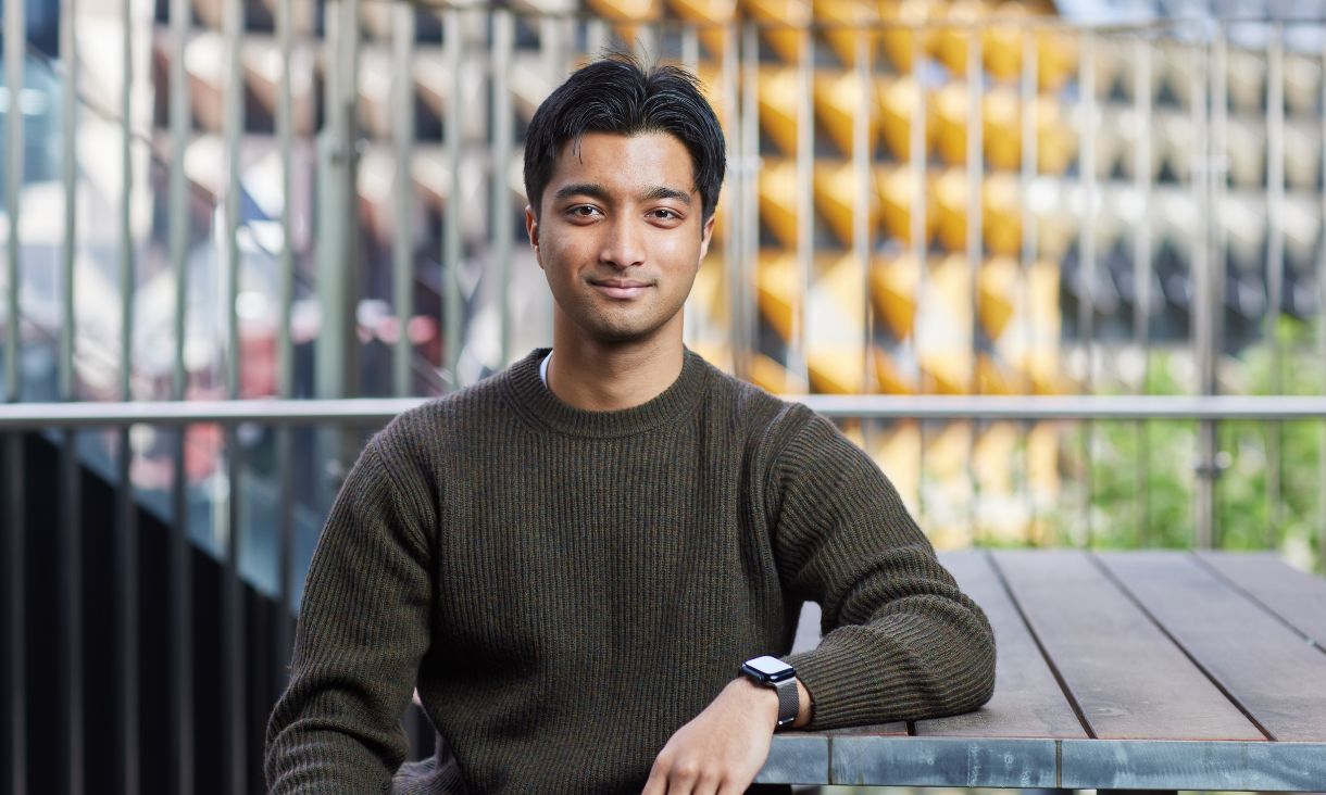 A student sitting oudoors at a wooden table.