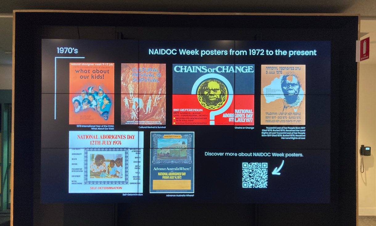A photo of a Library digital display screen showing NAIDOC posters from 1970s.