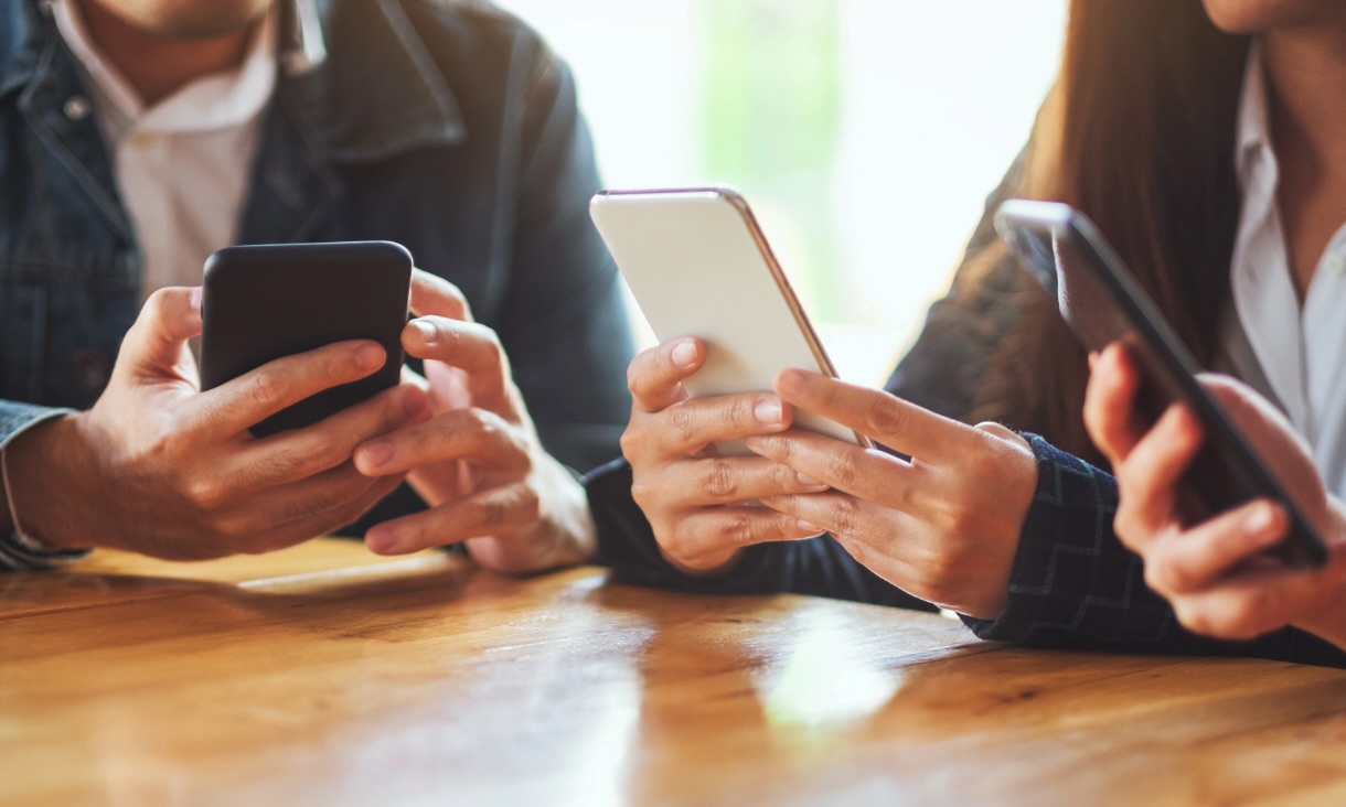 Close up of 3 people holding phones