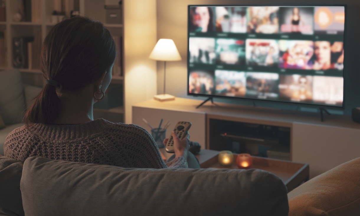 Woman sitting on couch in living room looking at television screen with a remote in her hand