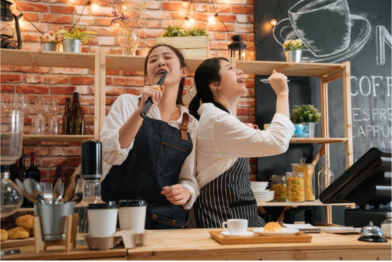 Two cafe workers lip synching with pretend microphones