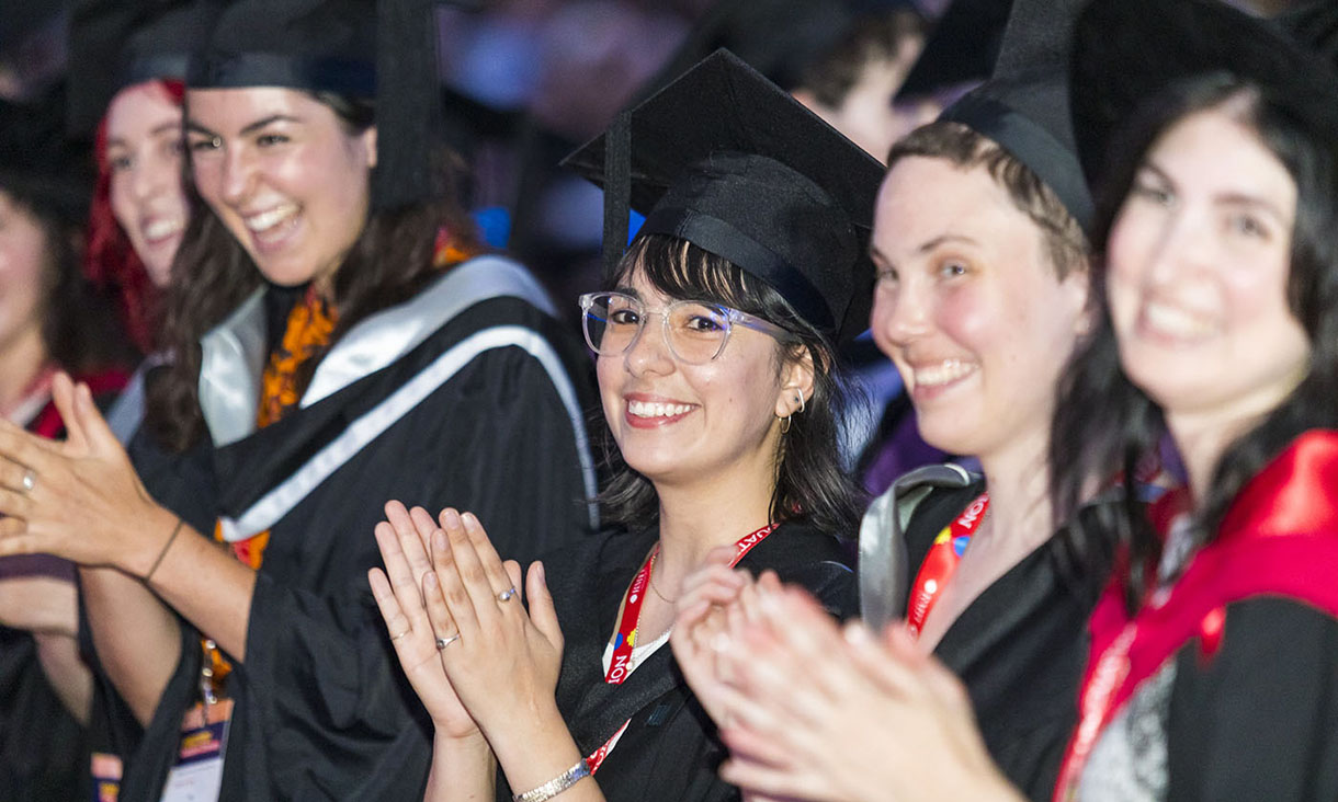 Group of female graduates applauding and smiling at the graduation ceremony