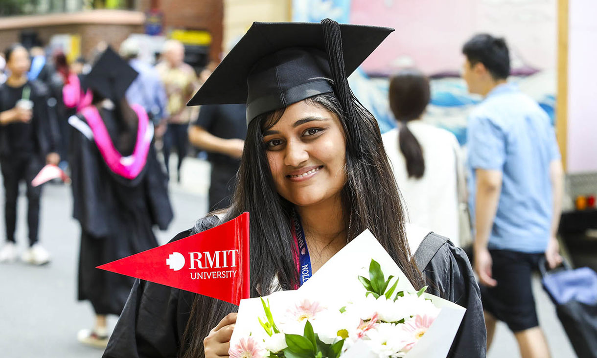 Female graduate looking at camera and holding a flag