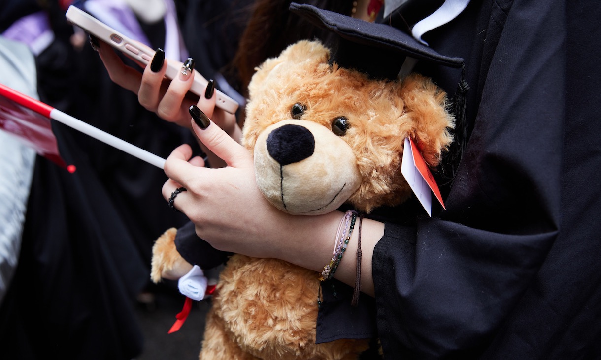 Graduation teddy bear held by student wearing graduation gown.