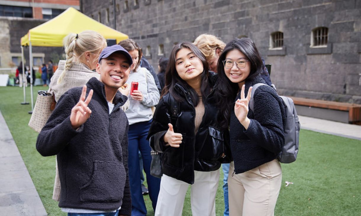 Three students smiling at camera and holding up peace hand symbol