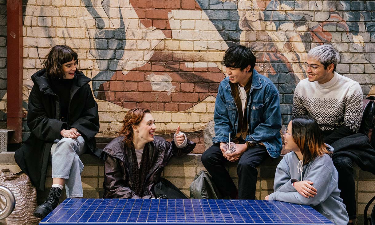 A group of students having a discussion on campus. One of them is doing a thumbs up gesture