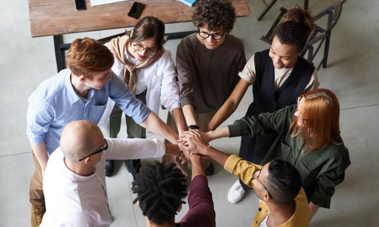 Group of people standing in a circle with outstretched hands in the centre