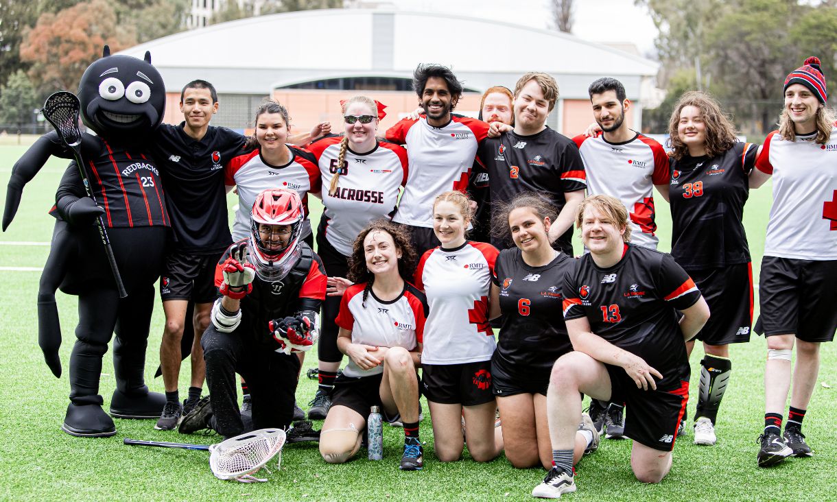 The lacrosse team posing with the redbacks mascot, a person in a cartoon spider outfit