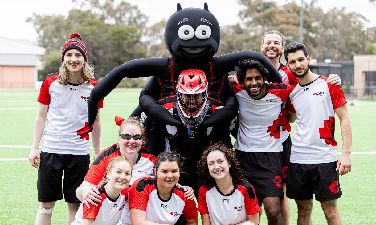 The Redbacks mascot is a cartoon spider and it's hugging a group of team members on a green playing field