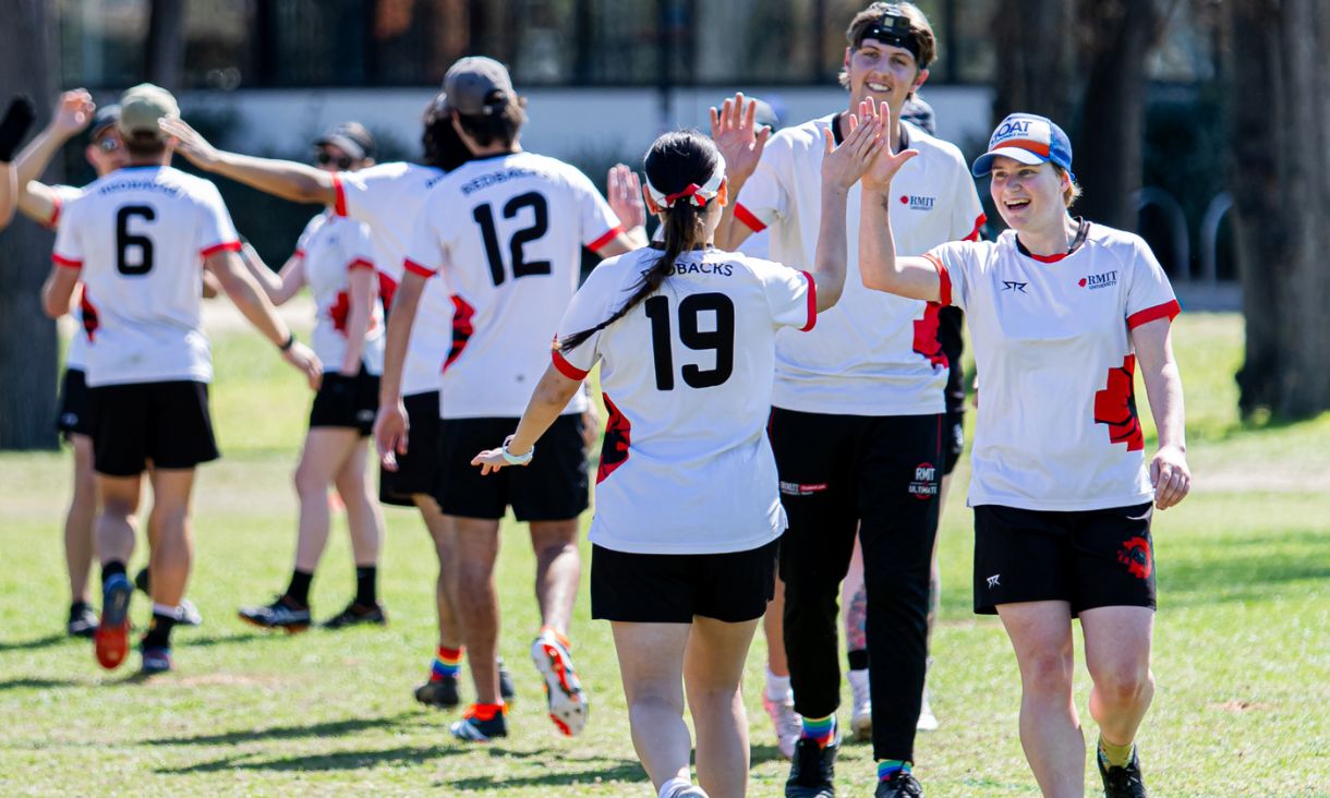 Two lines of players in Redbacks uniforms give each other high fives on a green field.