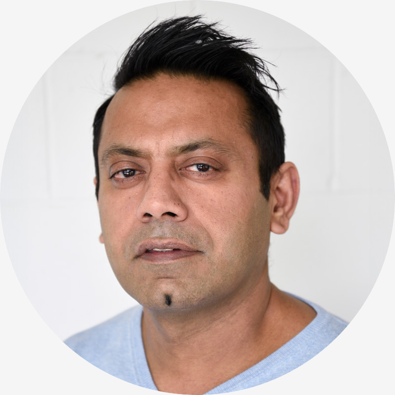 Portrait of Shekhar Kalra, he has tanned skin, black hair, brown eyes, and is wearing a grey t-shirt.