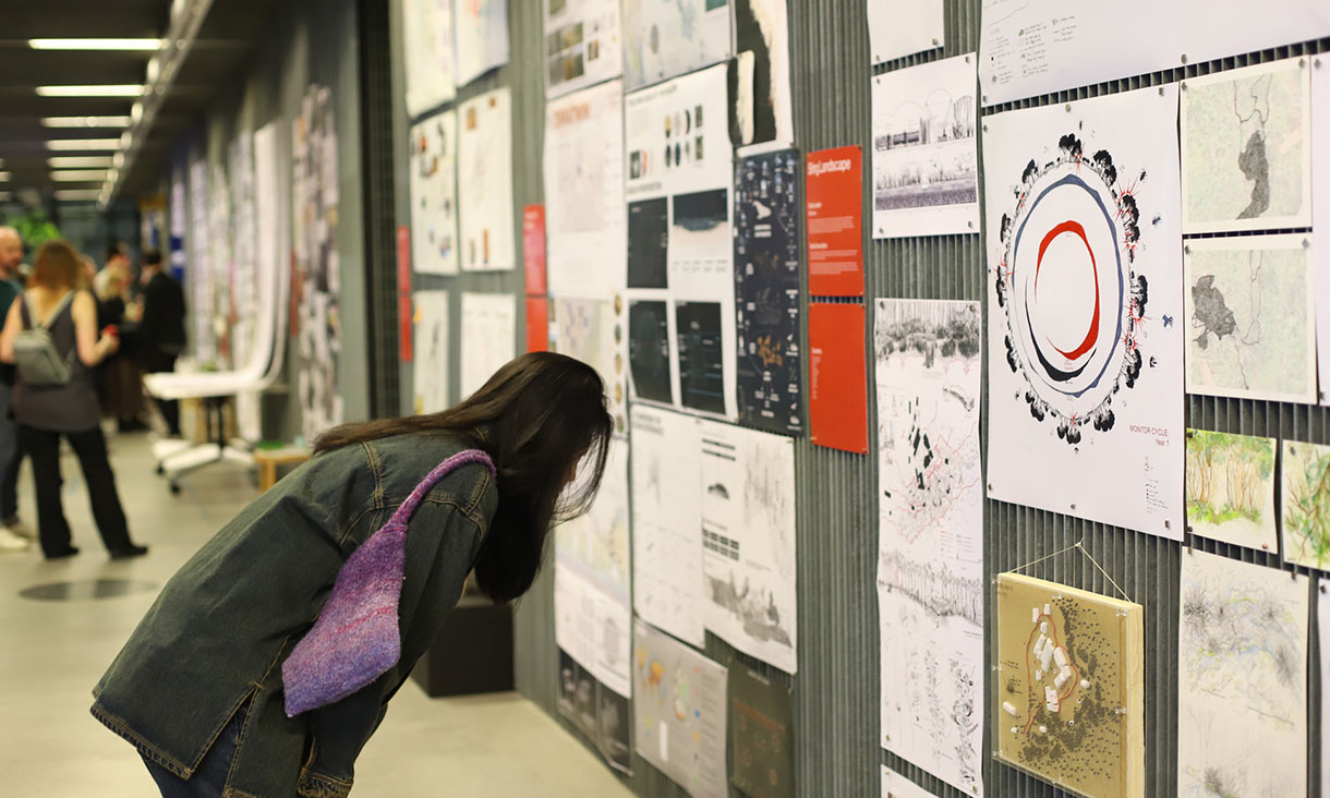 A woman with dark hair leans down to look at the landscape architecture exhibition submissions.