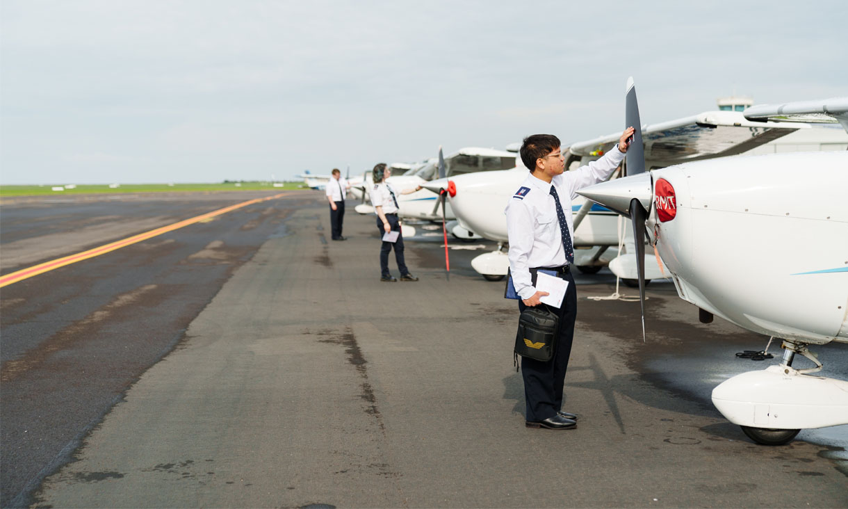 Three RMIT students dressed in pilot's uniforms examine the propellers on their respective planes.