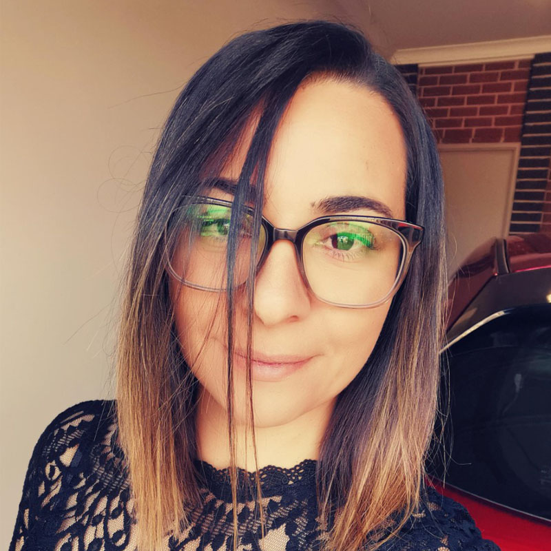 Headshot of Jessica Costa, she wears glasses, a black lace shirt, and has shoulder-length dark brown hair with blonde highlights.