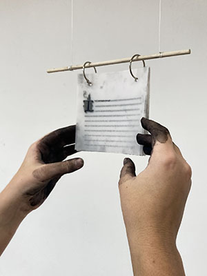 Ink-stained hands reaching for translucent paper hanging from a bar.