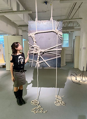 A person rests their hand on a suspended piece of steel wrapped in knotted rope.