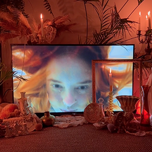 A screen showing a person underwater sits behind an array of objects including a vase, candle holders and an empty picture frame.