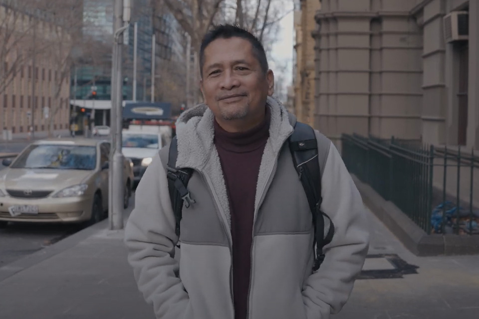 Azlan walks down a Melbourne street wearing a grey jacket, and maroon shirt.