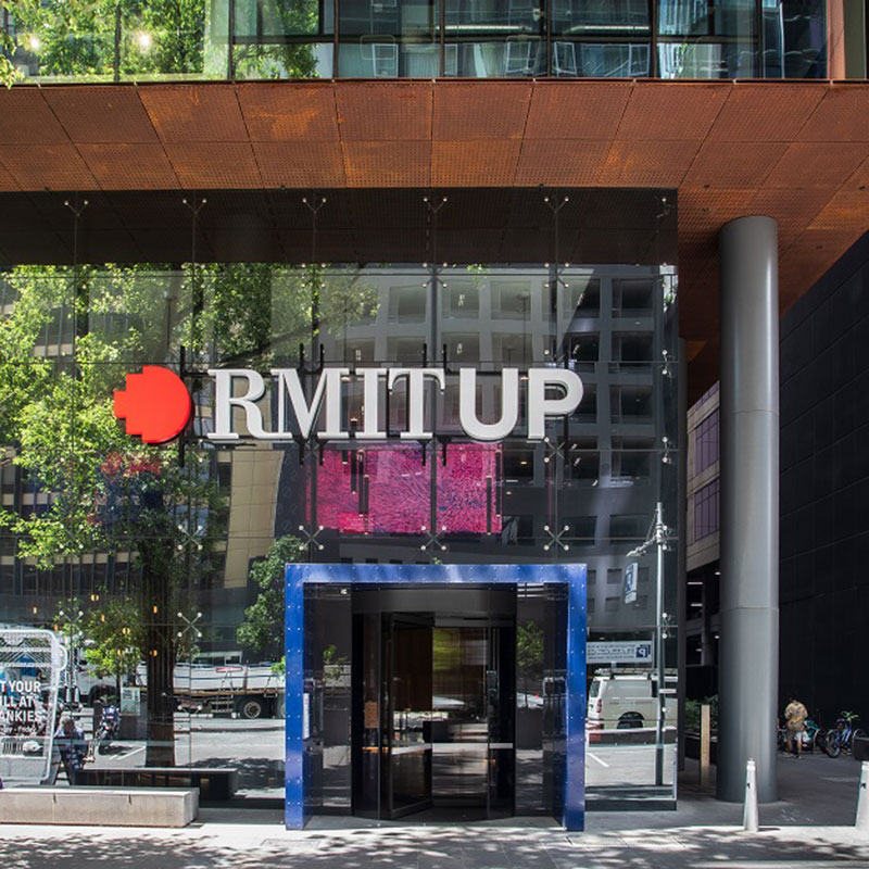 Facade of a building with large door outlined in blue and large RMIT UP sign above it.