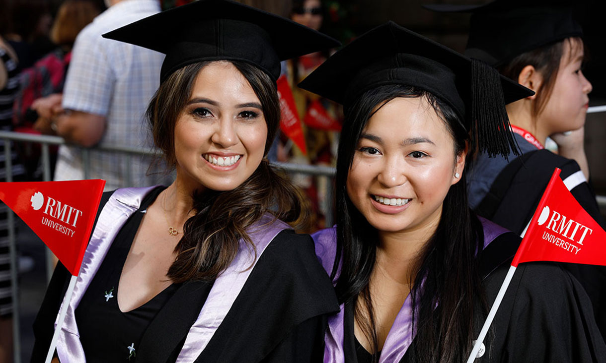 Two female graduates smiling and holding RMIT University flags