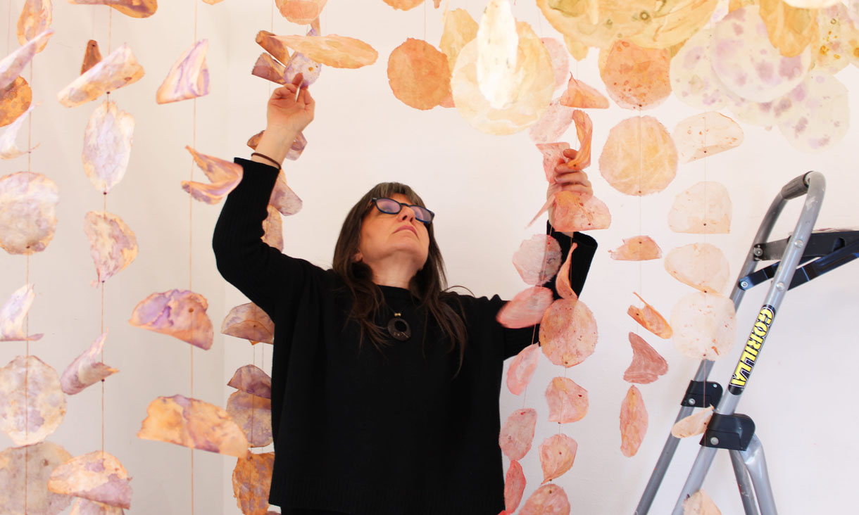 Angela puts together tengucho paper circles stained with foraged pigments and dyes, cotton thread, and wooden beads.