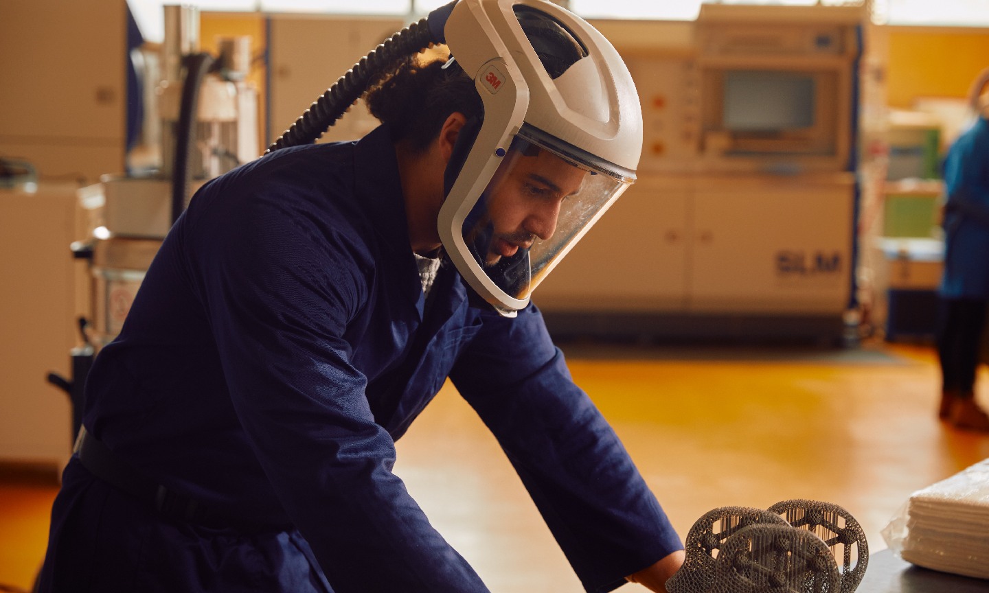 A postgraduate engineering student wearing safety equipment looks at an engineering sculpture