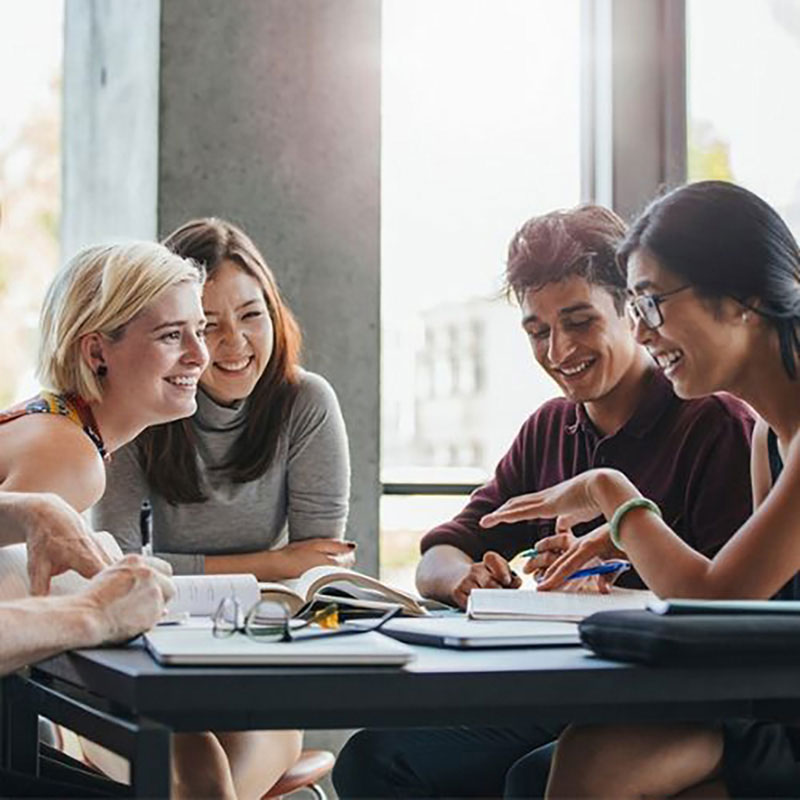 A group of four students is sitting at a table with open books.