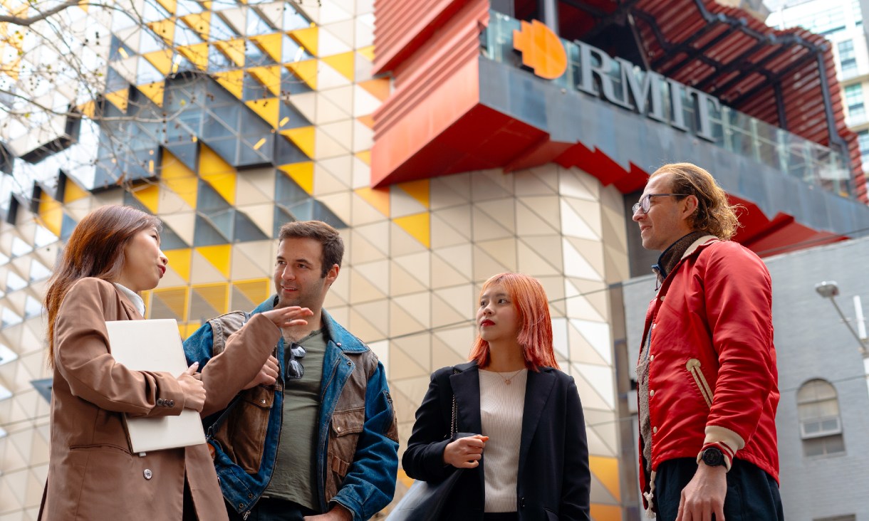 Four postgraduate students stand in front of Building 80 on the RMIT city campus