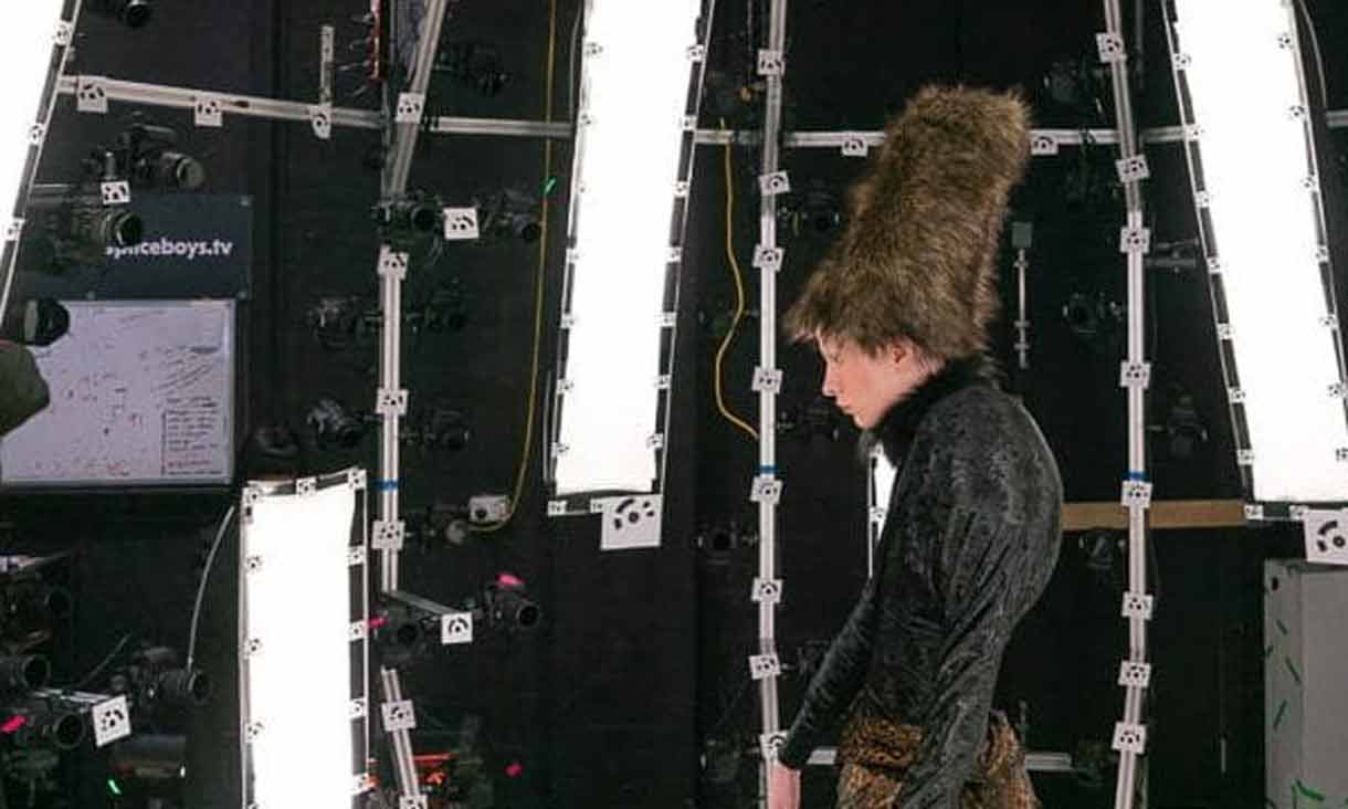 a figure wearing a black short, brown skirt and tall brown fluffy hat stands within a photogrammetry rig consisting of bars and cameras.