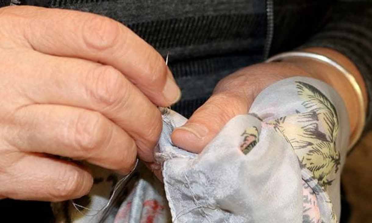 a close-up photograph of two hands embroidering a textile