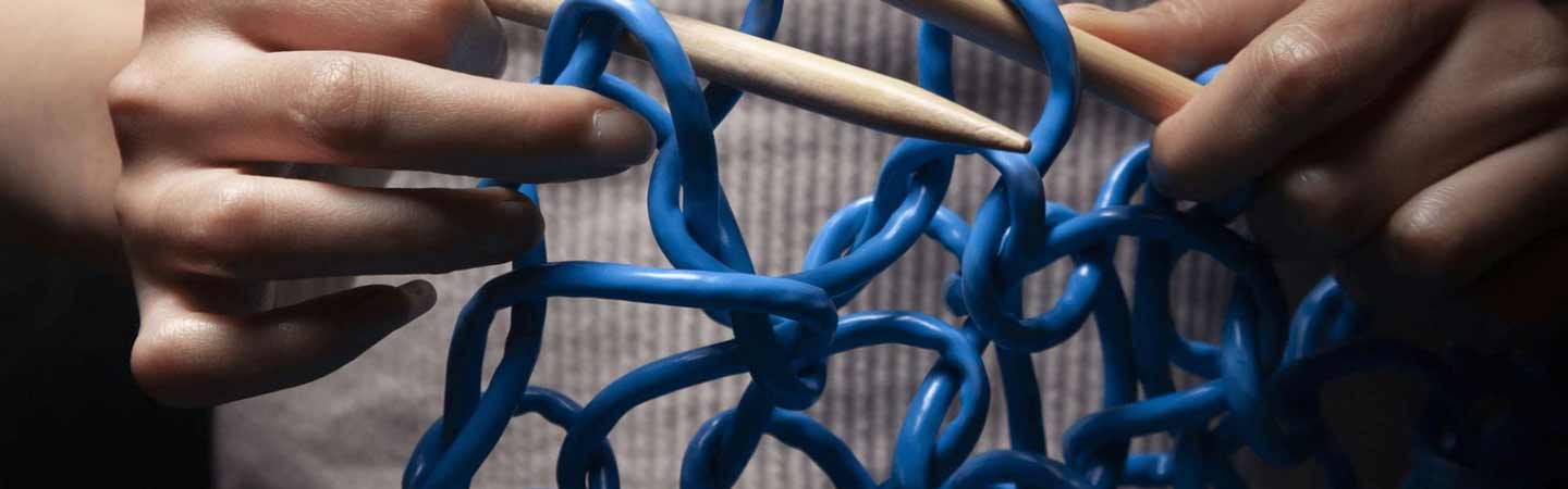 hands knitting blue plastic cord with thick wooden knitting needles. 