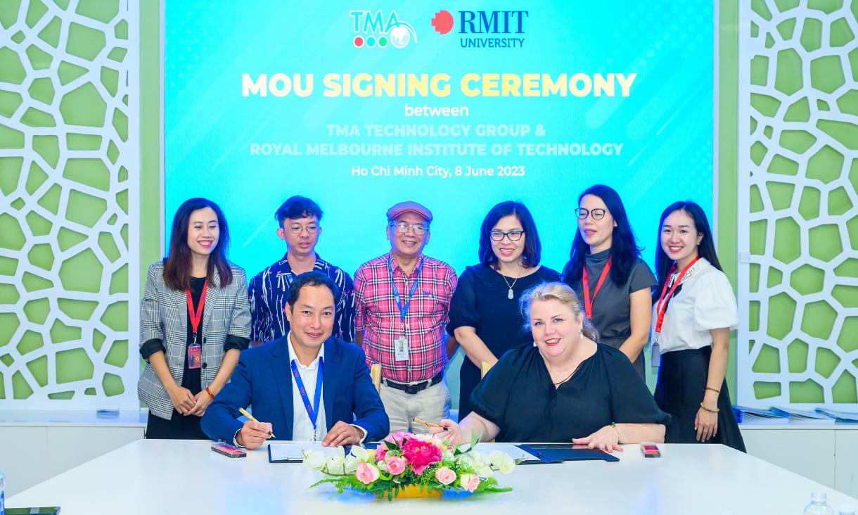 6 people stand behind Mish Eastman and Bui Duc Quang as they sign the MOU