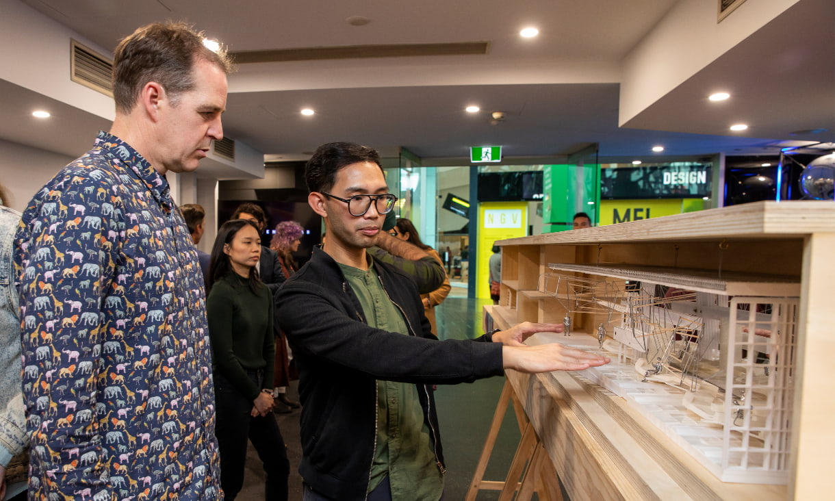 2 men stand next to a model of an art structure