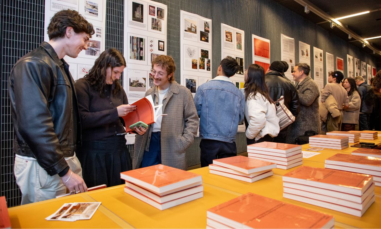 People looking at posters on a wall and flipping through copies of the book.