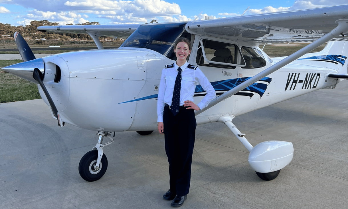 Amber is wearing her aviation uniform and is standing in front of a small plane