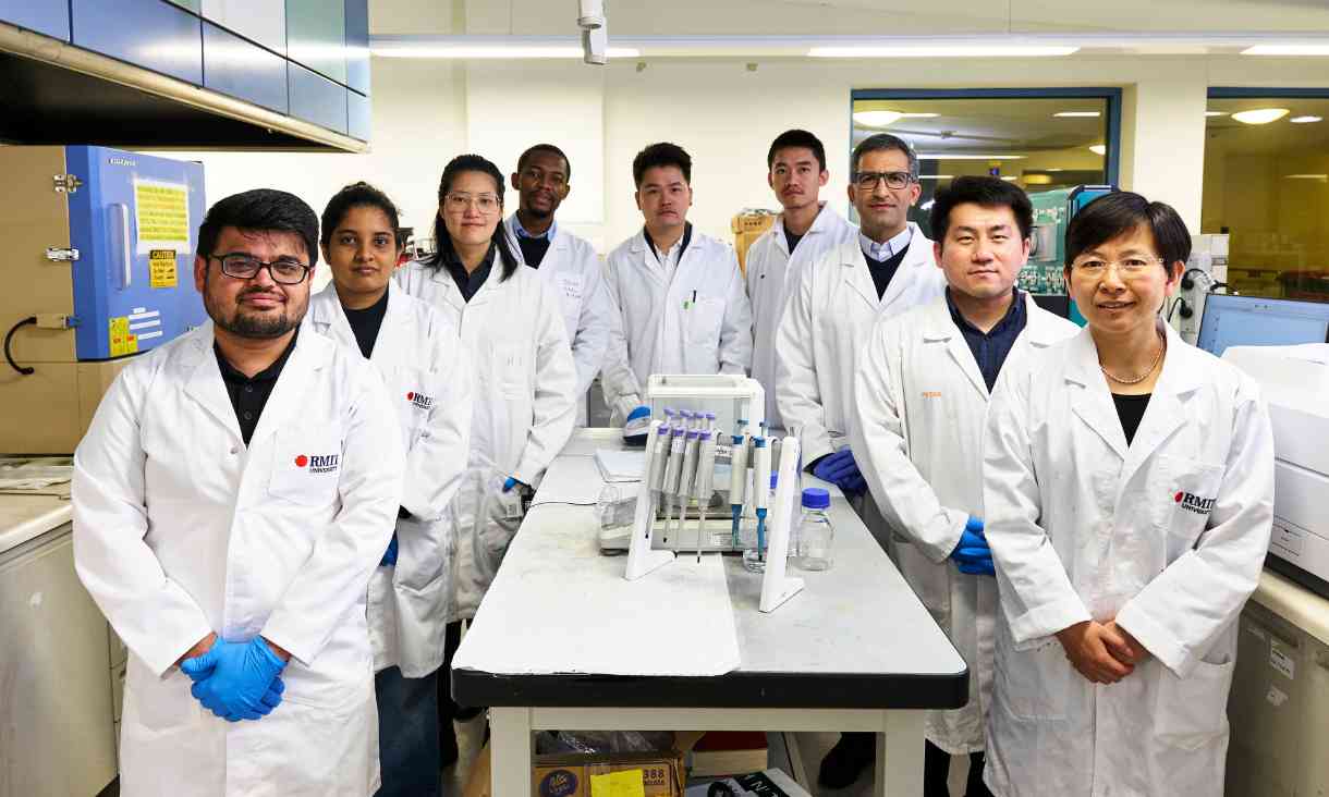 Research team pictured around workbench in lab wearing lab coats