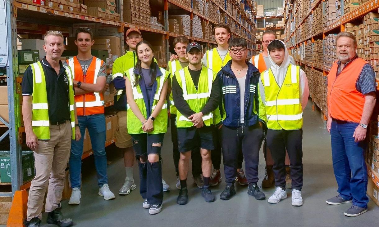 Group of students and teachers wearing hi-vis vests in warehouse