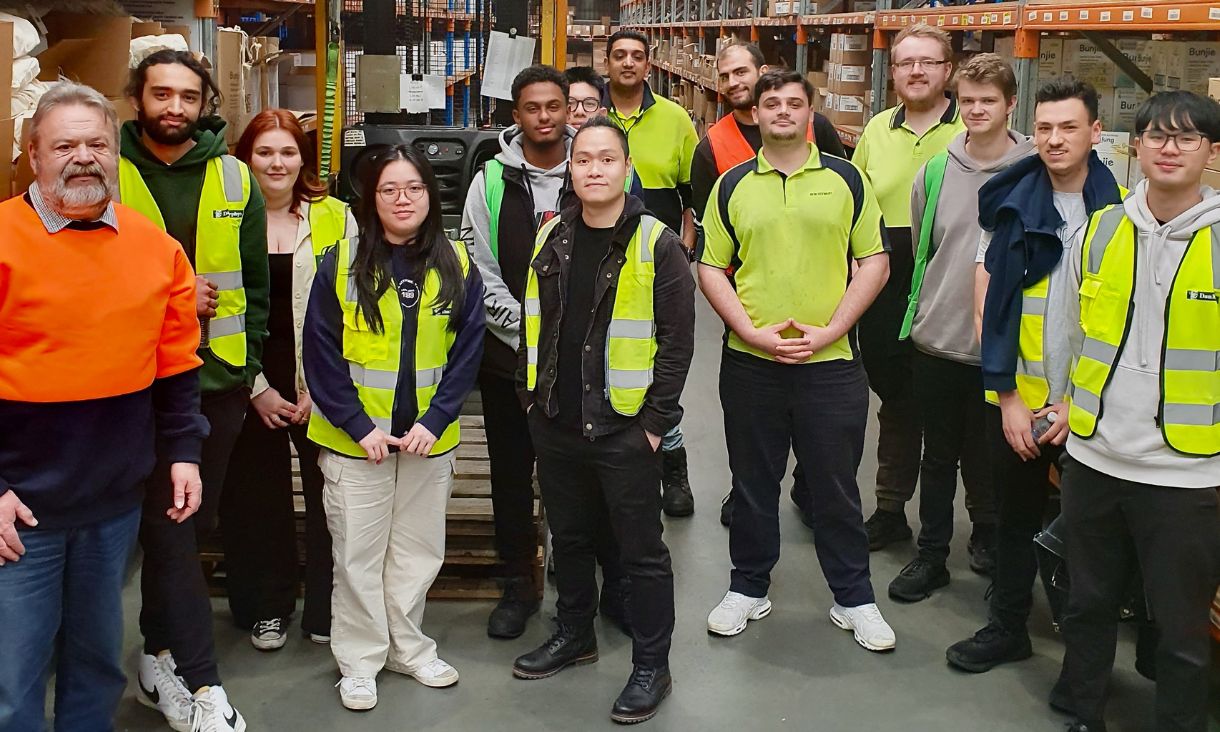 Group of students and teachers wearing hi-vis vests in warehouse