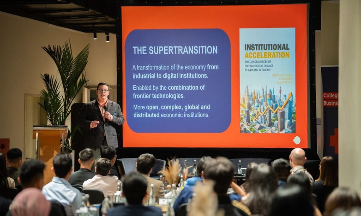 Dr. Darcy Allen on stage in front of PowerPointPowerPoint slide reading 'The Supertransition'