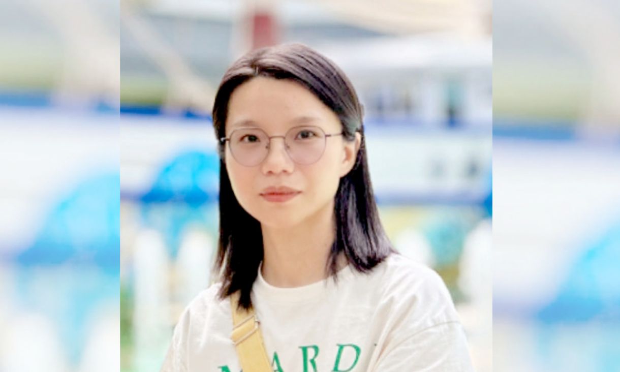 Woman with shoulder-length black hair and glasses posing against blurry blue background