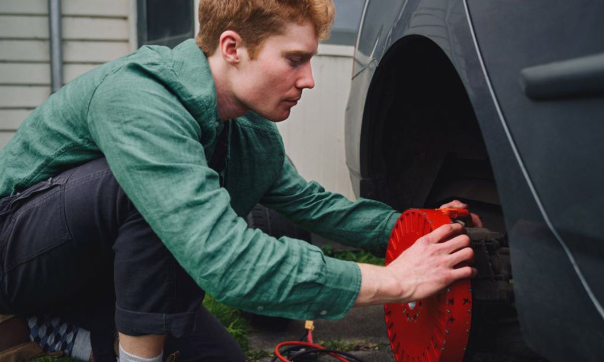 Man in green shirt placing red object on car tyre.