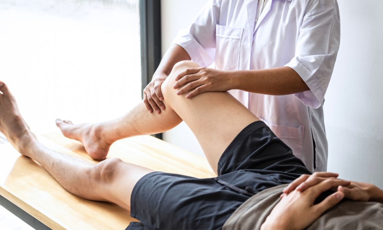 Stock image of man lying on table with bent knee that is being massaged.