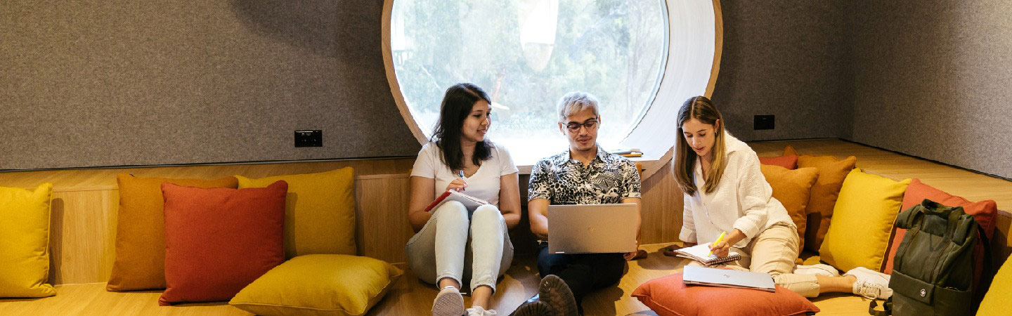 A male and female student in discussion with a female tutor, in front of a laptop screen